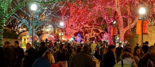 A vibrant holiday scene with colorful lights on trees, crowds of people enjoying the festive atmosphere.