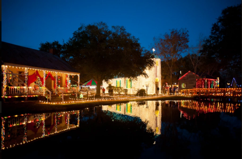 A festive scene of houses decorated with colorful lights, reflecting on a calm pond at night.
