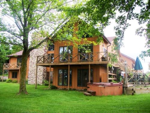 A wooden house with large windows, balconies, and a hot tub, surrounded by green grass and trees.