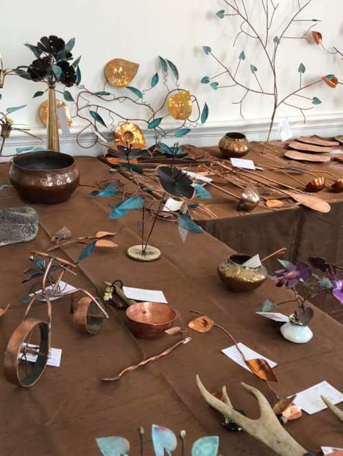 A display of handcrafted metal art, including flowers, leaves, and decorative items on a brown tablecloth.
