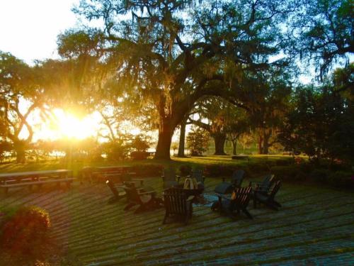 Sunset view over a serene garden with wooden chairs arranged around a fire pit, surrounded by trees and greenery.