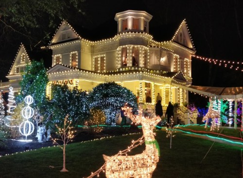 A beautifully decorated house with colorful Christmas lights and a glowing reindeer in the foreground.