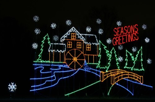 Colorful holiday lights depict a snowy scene with a house, trees, a river, and the words "SEASONS GREETINGS."