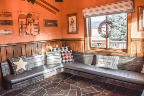 Cozy corner with a wooden bench, decorative pillows, and framed art, illuminated by natural light from a window.