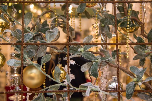 A close-up of mistletoe and festive decorations, with golden beads and ornaments in a blurred background.