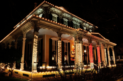 A beautifully lit historic house at night, adorned with festive lights and decorations.