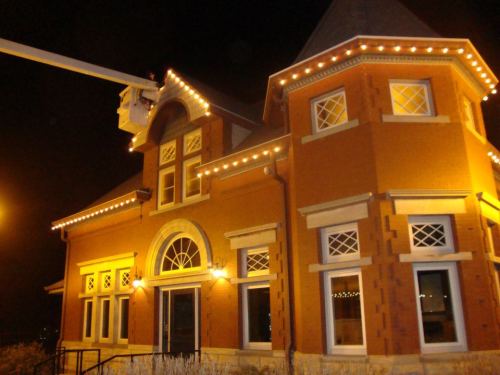 A brightly lit historic building at night, adorned with string lights and featuring a turret and large windows.