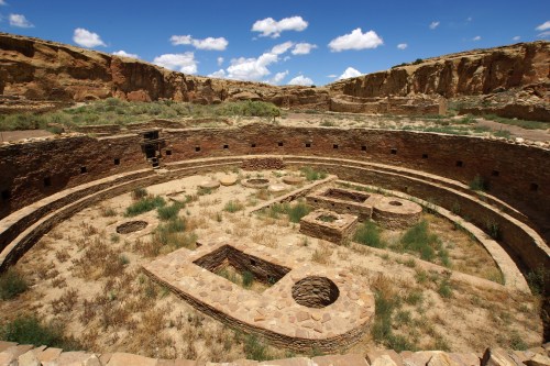 Ancient circular ruins surrounded by desert landscape and blue sky, with remnants of stone structures visible.