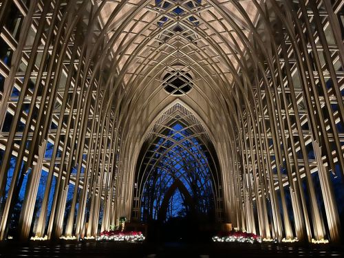 A stunning interior of a modern church with intricate wooden arches and soft lighting against a twilight sky.