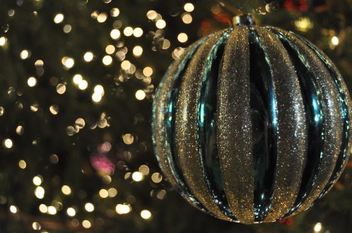 A shiny, striped ornament hangs on a Christmas tree, with blurred lights in the background.