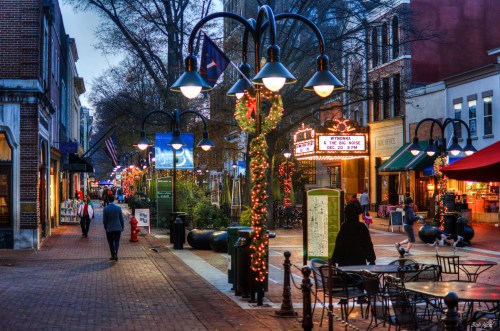 A lively street scene with festive lights, shops, and people walking along a brick pathway in a charming urban area.