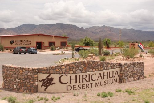 Sign for Chiricahua Desert Museum with mountains in the background and a parking area in front.