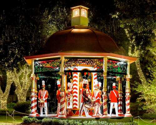 A festive gazebo with colorful decorations and toy soldiers playing drums, illuminated by twinkling lights at night.