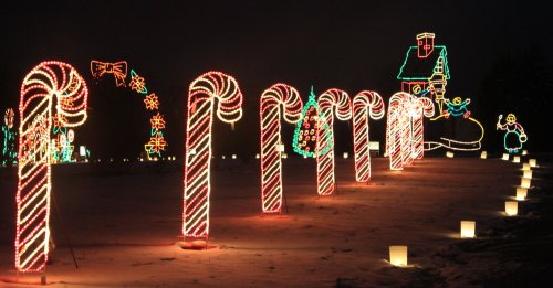 Colorful holiday lights shaped like candy canes, with festive decorations and a house in the background at night.