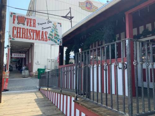 Sign reading "Flower Christmas" hangs above a wooden deck with festive decorations in a market setting.