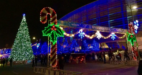A festive scene with a large illuminated Christmas tree, candy cane decorations, and snowflakes, bustling with people at night.