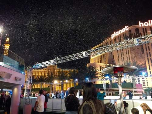 A lively night scene at Planet Hollywood, with people enjoying the atmosphere and artificial snow falling.
