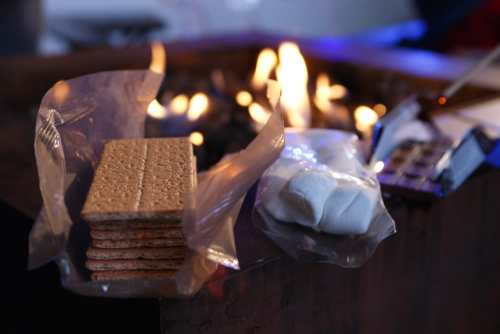 Graham crackers, marshmallows, and chocolate near a fire, ready for making s'mores.