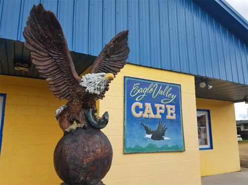 A large eagle statue stands on a globe in front of the Eagle Valley Cafe, with a colorful sign on the building.
