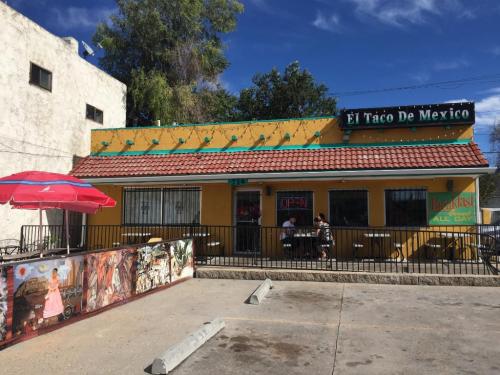 A colorful restaurant exterior with a sign reading "El Taco De Mexico," featuring outdoor seating and a vibrant mural.