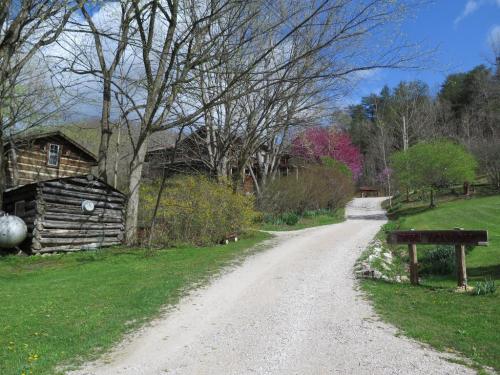 A gravel road leads through a lush green landscape with trees and rustic buildings under a partly cloudy sky.