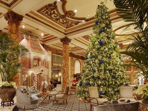 A beautifully decorated hotel lobby featuring a large Christmas tree and a festive gingerbread house.