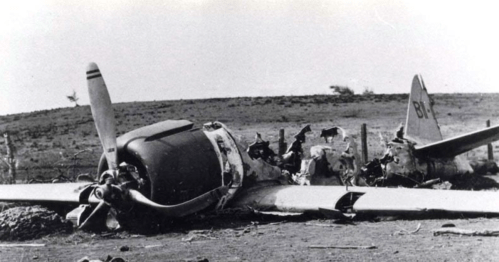 A crashed vintage airplane lies in a barren landscape, with visible damage to its fuselage and propeller.