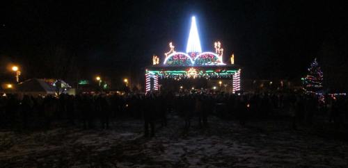 A festive scene at night with a large illuminated structure and a crowd, surrounded by holiday lights and decorations.