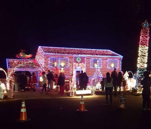 A brightly lit house decorated with colorful Christmas lights, with people admiring the festive display outside.