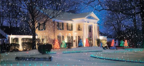 A beautifully lit house decorated for Christmas, surrounded by colorful trees and falling snow at night.