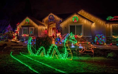 A house decorated with colorful Christmas lights, featuring a green dragon made of lights in the front yard.