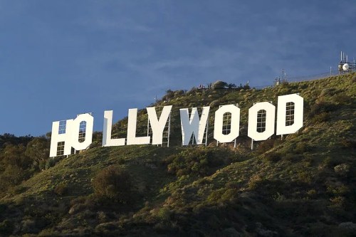 The iconic Hollywood sign on a hillside, partially obscured by greenery, against a blue sky.