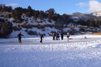 People ice skating and playing in a snowy landscape with mountains in the background.