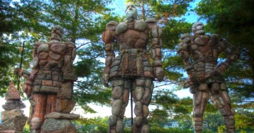 Three large stone sculptures of armored figures stand among trees, showcasing intricate details and a natural setting.