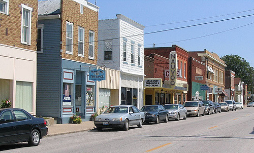 A quaint street lined with small shops and parked cars under a clear blue sky.
