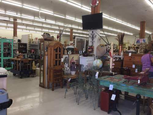 A spacious thrift store filled with various vintage furniture and decor items, including tables, chairs, and shelves.