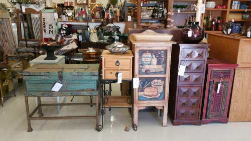 A display of various vintage furniture pieces, including a green chest, wooden cabinets, and decorative items.