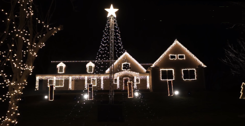 A beautifully decorated house with bright Christmas lights and a tall star atop a tree, set against a dark night sky.