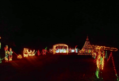 A festive display of colorful Christmas lights, featuring a tree, train, and various decorations against a dark night sky.