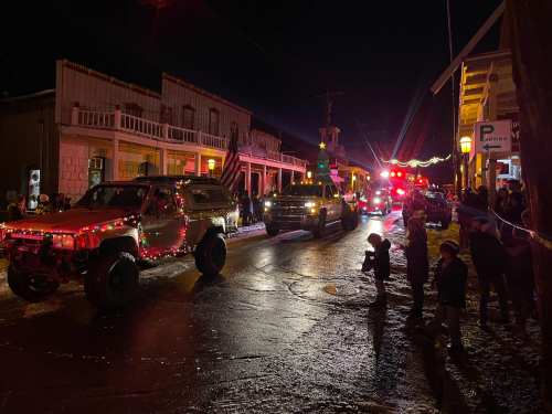 A nighttime parade with decorated vehicles and emergency lights, lined by spectators on a festive street.