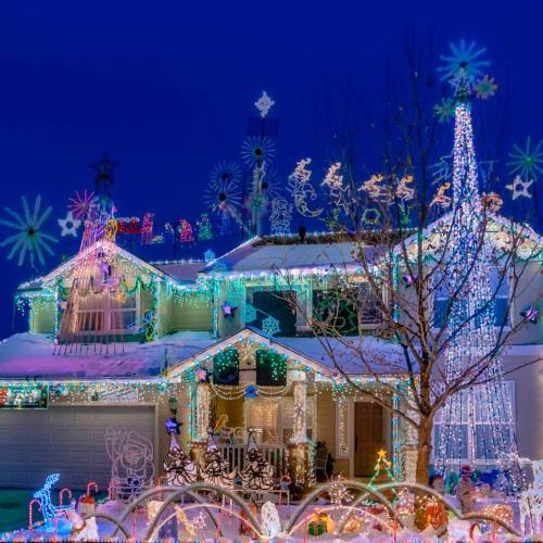 A brightly lit house decorated with colorful holiday lights and festive decorations, set against a dark evening sky.