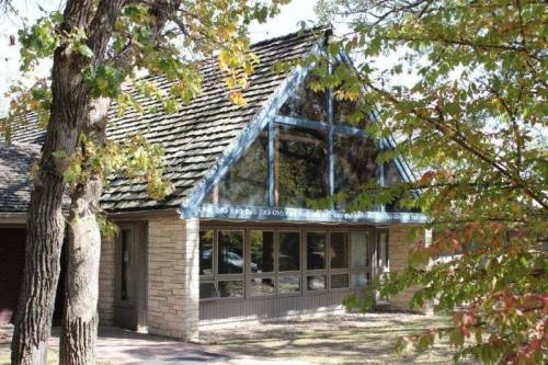 A charming house with a sloped roof, large windows, and surrounded by trees with autumn leaves.