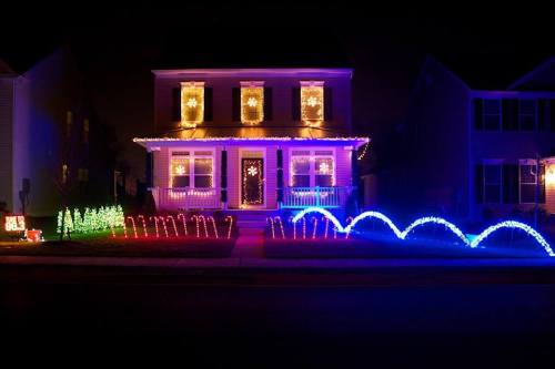 A brightly lit house decorated with colorful Christmas lights, featuring snowflake designs and illuminated trees in the yard.