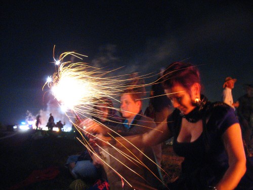 A group of people enjoying a night outdoors, with one person holding a sparkler that creates bright trails of light.