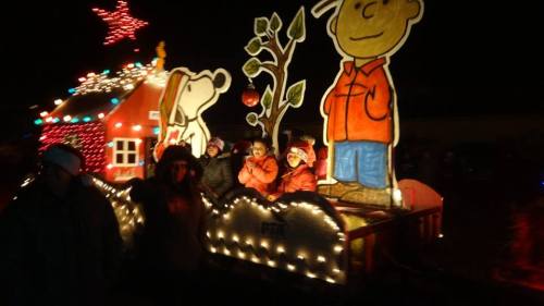 A festive parade float featuring cartoon characters, colorful lights, and children in winter attire, celebrating the holiday season.