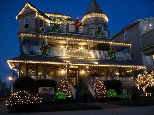 A beautifully decorated house with festive lights and wreaths, glowing warmly against a twilight sky.