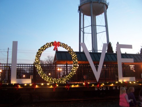 Large "LOVE" sign decorated with a wreath and lights, set against a twilight sky and a water tower in the background.