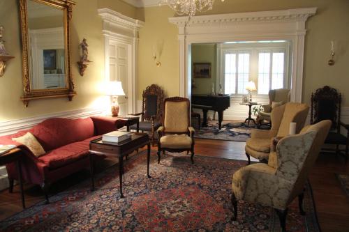 A cozy living room with a red sofa, elegant chairs, a piano, and a decorative rug under soft lighting.