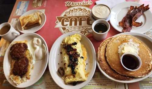 A breakfast spread featuring pancakes, an omelet, sausage, bacon, toast, and coffee on a cafe table.