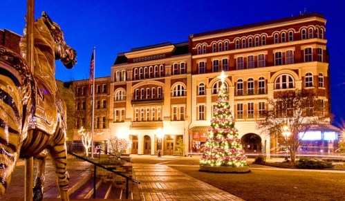 A festive scene featuring a decorated Christmas tree and a historic building, illuminated at night with a golden horse statue.